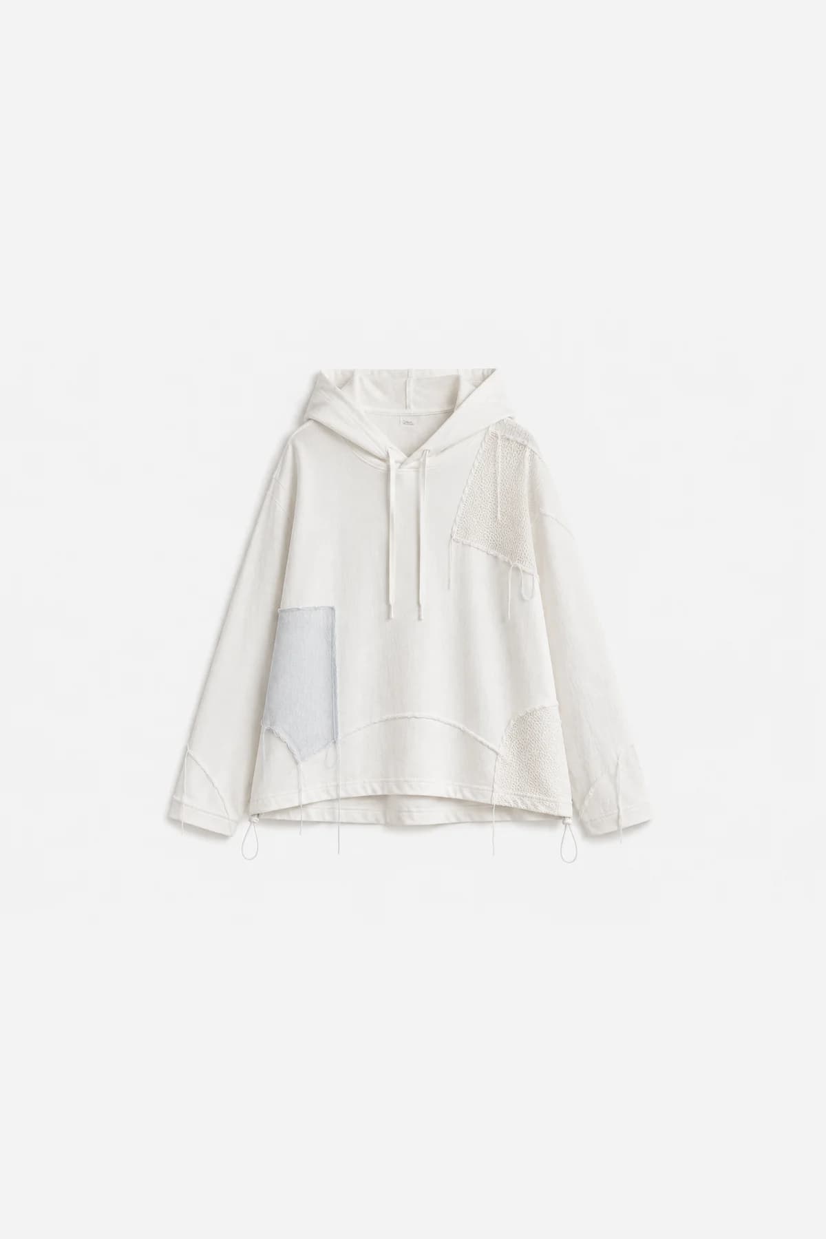 Ivory pullover hoodie laid flat, mesh and fabric patches pieced across the chest and sleeve