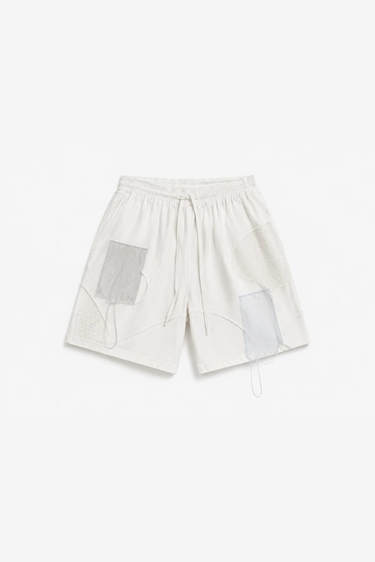 White drawstring shorts laid flat, mesh and fabric patches pieced at the hip and thigh