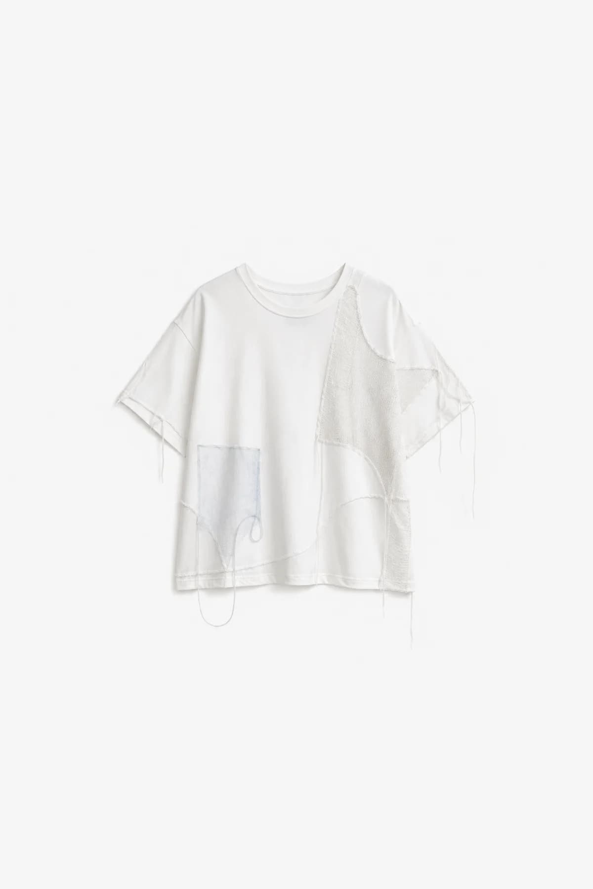 White oversized tee laid flat, a mesh panel and fabric patch pieced across one side