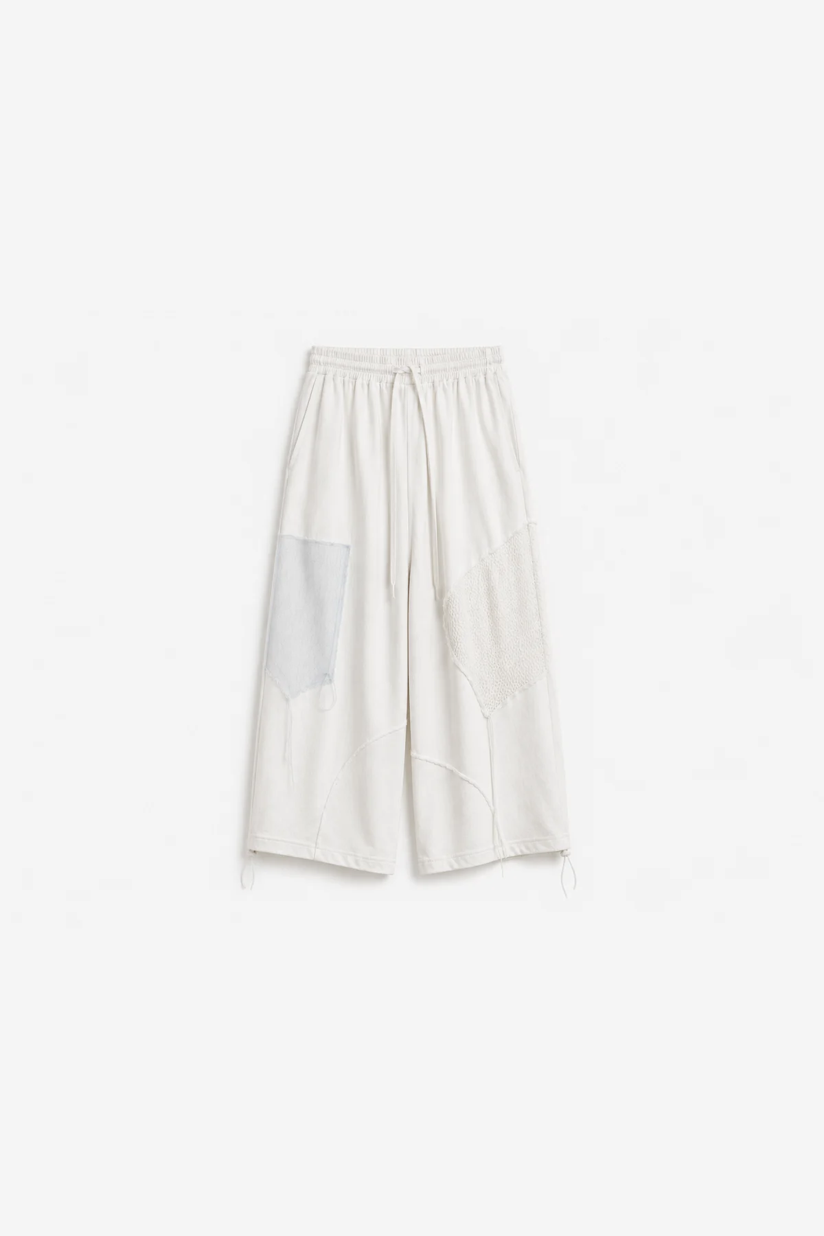 Ivory wide-leg trousers laid flat, mesh and fabric patches pieced at the thigh